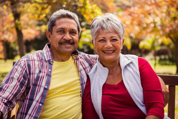 Una pareja de ancianos sonriendo a la cámara sentada en el banco