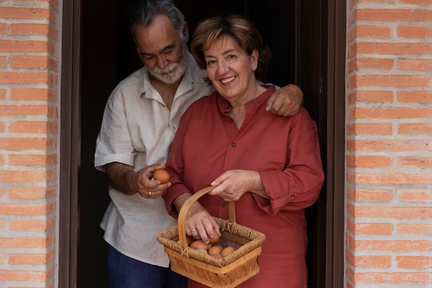 Foto pareja de ancianos sosteniendo huevos del granero de su casa de campo