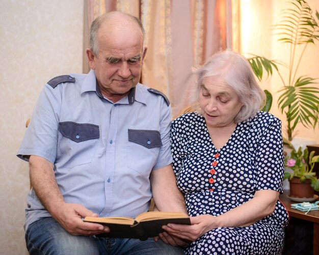 Una pareja de ancianos sosteniendo un libro y leyéndolo juntos en casa