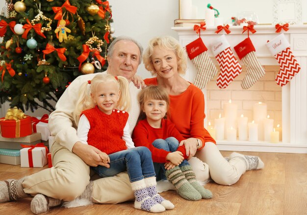 Pareja de ancianos con sus nietas sentado junto a la chimenea decorada para Navidad