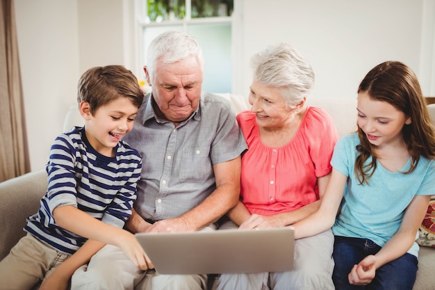 Pareja de ancianos y sus nietos usando una computadora portátil en la sala de estar