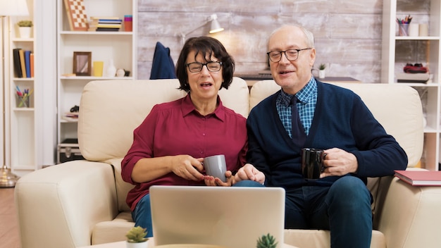 Pareja de ancianos con tecnología moderna. Están en una videollamada usando una computadora portátil.