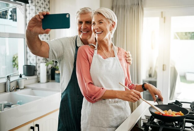 Una pareja de ancianos toma selfie por teléfono y cocina en la cocina deliciosa comida y comida en casa Amor sonrisa y feliz anciano jubilado romántico hombre y mujer cocinan el desayuno por la mañana y toman fotos juntos