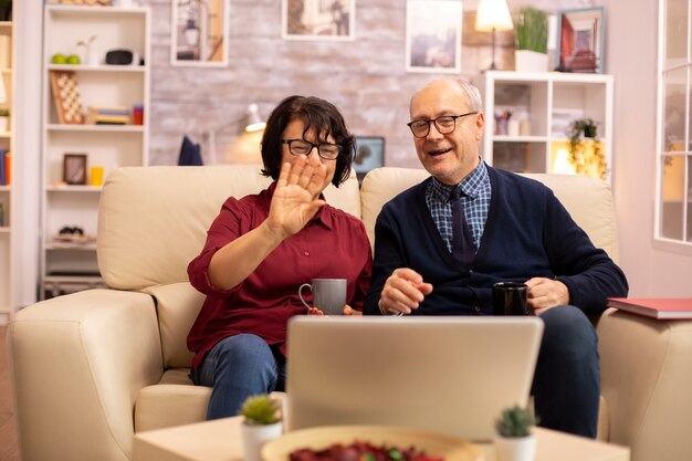 Pareja de ancianos usando una computadora portátil moderna para charlar con su nieto. Abuela y abuelo con tecnología moderna.