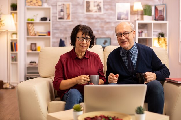 Pareja de ancianos usando una computadora portátil moderna para charlar con su nieto. Abuela y abuelo con tecnología moderna.