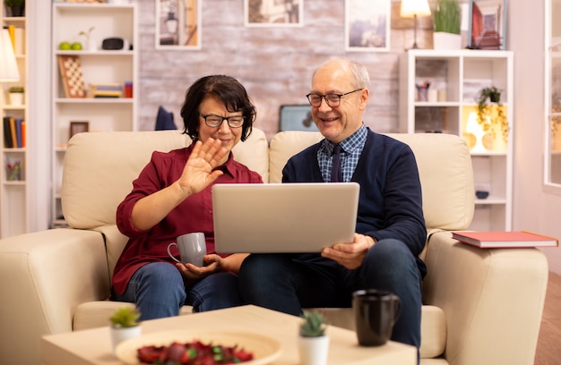 Pareja de ancianos usando una computadora portátil moderna para charlar con su nieto. Abuela y abuelo con tecnología moderna.