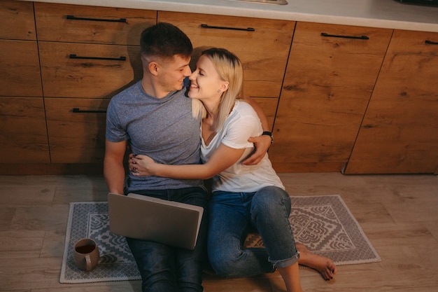 Pareja animando juntos en la cocina en el piso mientras toma un café y usa la computadora