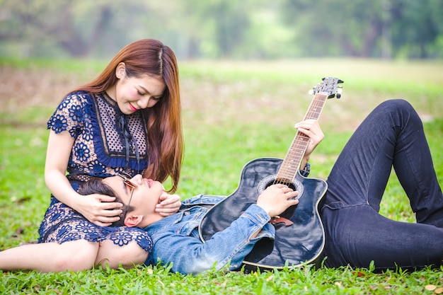 Pareja asiática en el amor tocando guitarra acústica canción sentada en la hierba en el parque