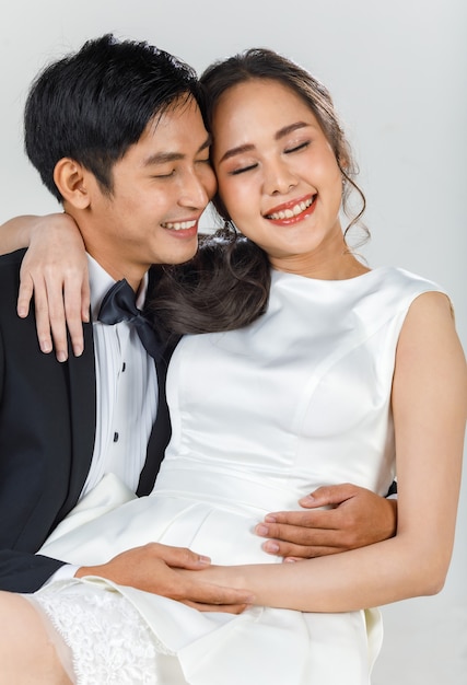 Pareja asiática atractiva joven, novios, mujer con vestido de novia blanco. Hombre vestido con esmoquin negro, abrazándose. Concepto de fotografía previa a la boda.