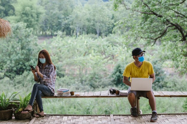 Pareja asiática Distanciamiento social y uso de máscaras protectoras trabajando, protección contra la enfermedad Coronavirus COVID-19. Conversación desde una distancia segura. Restricción de socialización.