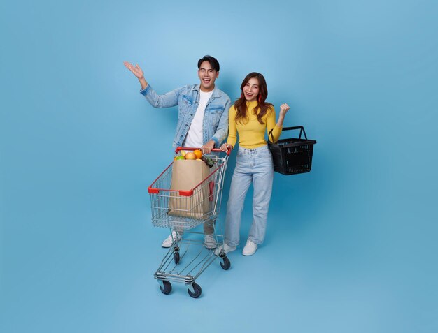 Una pareja asiática se divierte conduciendo un carrito de compras y sosteniendo una bolsa de compras en el supermercado.