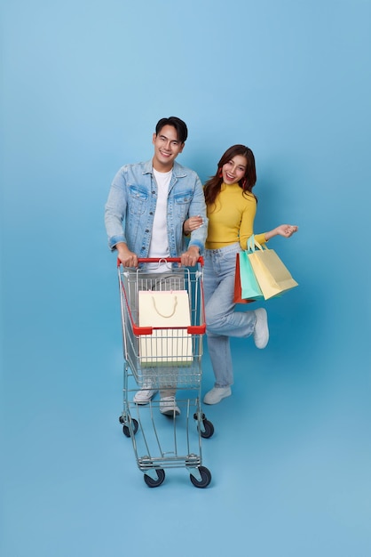 Una pareja asiática se divierte conduciendo un carrito de compras y sosteniendo una bolsa de compras en un supermercado.