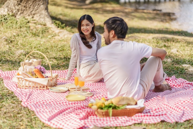Foto pareja asiática enamorada disfrutando de un picnic en el parque al aire libre pareja feliz de picnic relajándose junto con una cesta de picnic