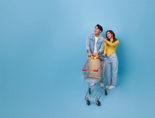 Una pareja asiática feliz empujando el carrito de compras señalando con el dedo la promoción en el supermercado