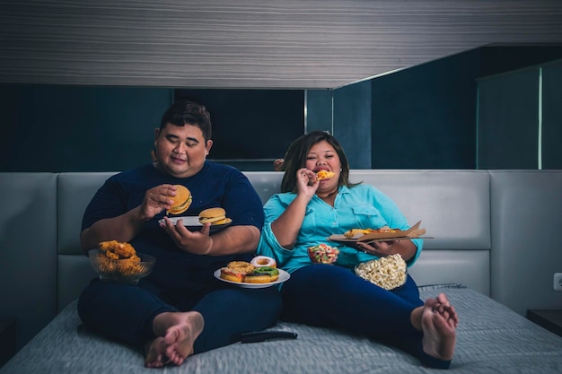 Pareja asiática gorda comiendo hamburguesa con queso y pizza