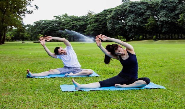 Pareja asiática sana y en forma practicando yoga al aire libre juntos en el parque con los brazos estirados.