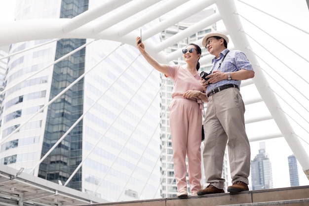 Pareja asiática senior selfie de pie por móvil al aire libre durante el día durante un viaje juntos en un hito en Tailandia. Concepto de viaje de pareja senior.