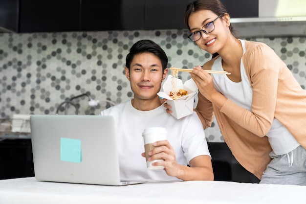 Pareja asiática trabaja desde casa en la cocina con entrega de comida para llevar