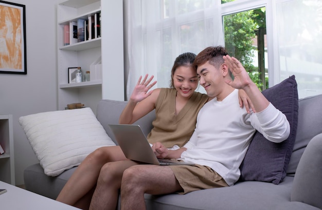 Pareja asiática usando una computadora portátil para conectarse con la familia para una videollamada Hombre y mujer usando una computadora portátil en la sala de estar en casa