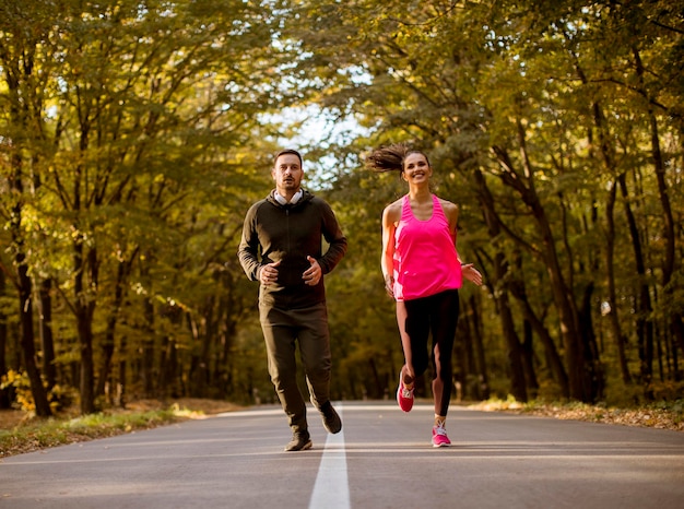 Pareja atlética corriendo juntos por el sendero del bosque