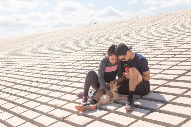 Pareja atlética descansando y acariciando a su cachorro en la orilla del mar.