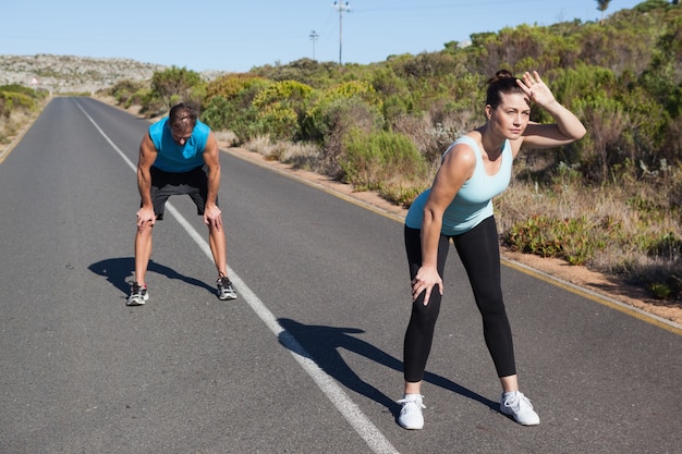 Pareja atlética tomando un descanso de correr en la carretera abierta