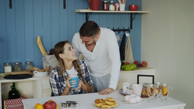 Una pareja atractiva se encuentra y se besa en la cocina a la hora del desayuno en casa