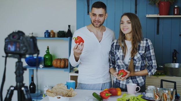 pareja atractiva grabando video blog sobre comida saludable en cámara dslr en la cocina en casa