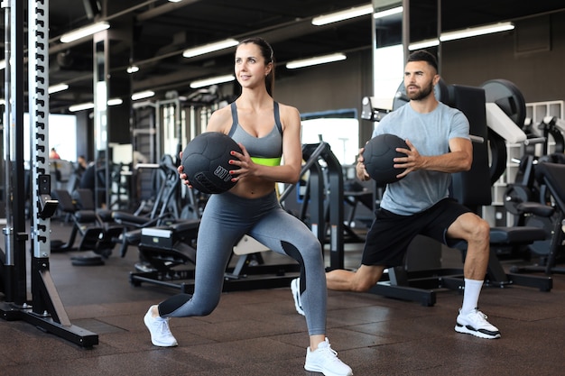 Pareja atractiva haciendo fitness con pelota medcine en el gimnasio.