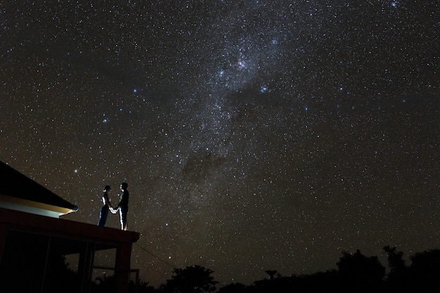 Pareja en la azotea mirando mliky way y estrellas en el cielo nocturno