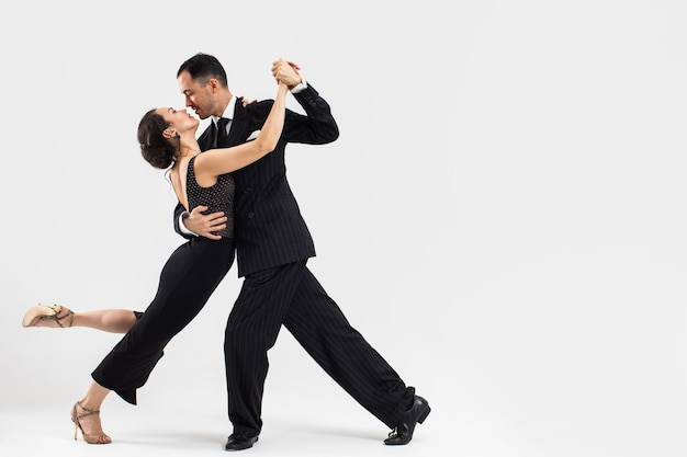 Pareja de bailarines de tango profesionales en traje elegante y vestido posan en un movimiento de baile. Atractivo hombre y mujer bailan cara a cara con amor y pasión sobre fondo blanco.