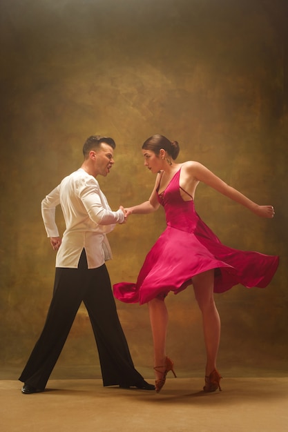 Pareja de baile de salón en vestido dorado bailando sobre fondo de estudio.