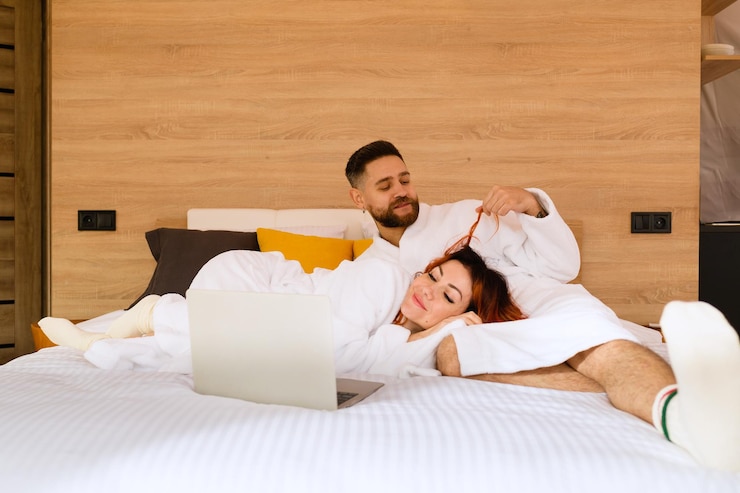 Foto pareja en batas de baño está acostada en la cama con una computadora portátil