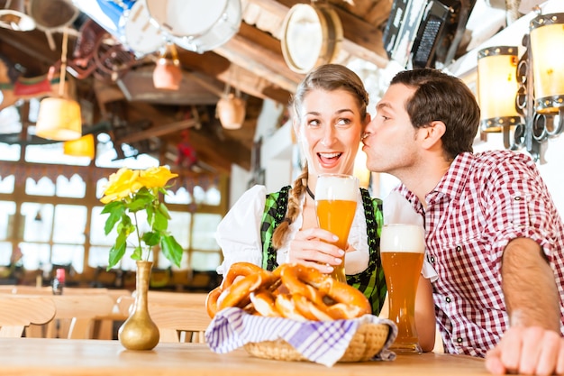 Pareja bávara vistiendo un traje tradicional, coqueteando y bebiendo cerveza en el restaurante