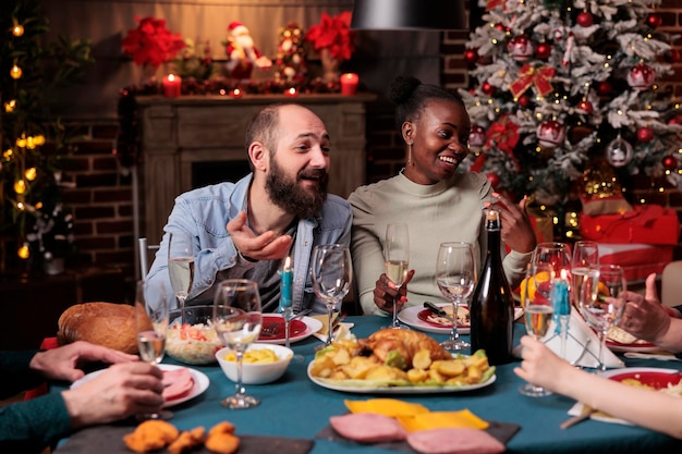 Pareja bebiendo vino espumoso en la cena festiva de navidad, proponiendo brindis, sosteniendo un vaso en la fiesta de navidad en casa. Familia joven celebrando las vacaciones de invierno, comiendo platos tradicionales en la fiesta de año nuevo