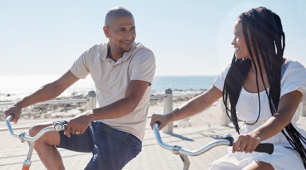 Pareja en bicicleta y playa para divertirse en una relación amorosa feliz en Ciudad del Cabo Sea Point Ciclismo fitness y vínculo con un hombre y una mujer montando en bicicleta junto al mar o el océano en verano