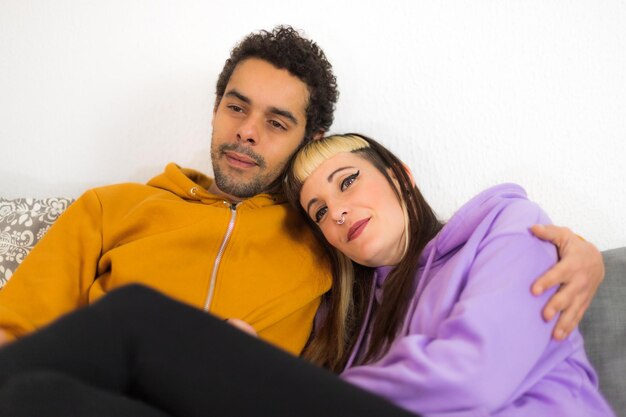 Una pareja biracial viendo la televisión relajada en el sofá de casa