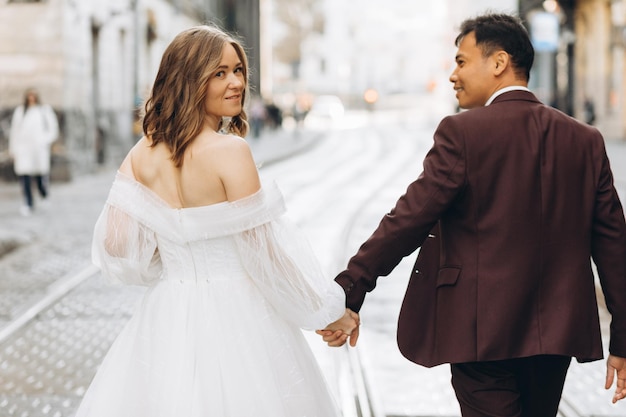 Una pareja de bodas internacionales, una novia europea y un novio asiático, caminan juntos por la ciudad