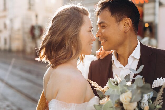 Una pareja de bodas internacionales, una novia europea y un novio asiático, caminan juntos por la ciudad