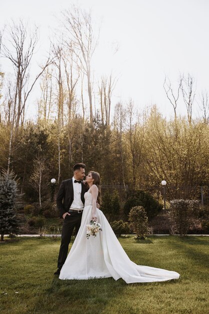 Una pareja de bodas internacionales, una novia europea y un novio asiático caminan por el parque