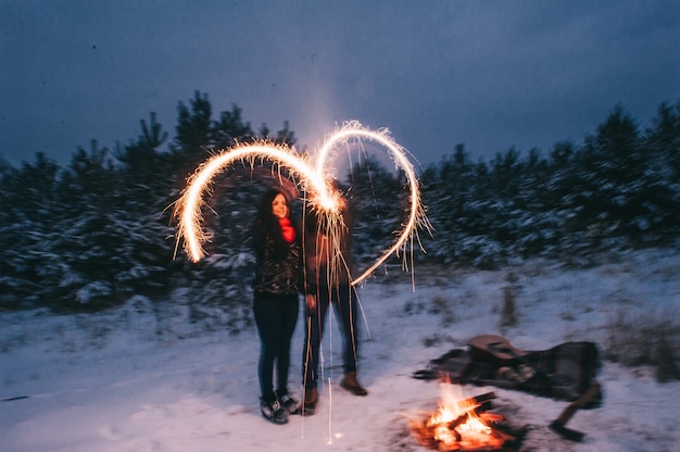 Pareja en un bosque de invierno con bengalas para el humor festivo.