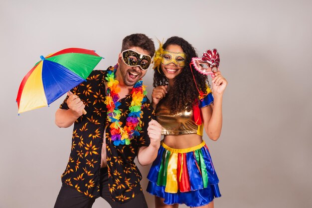 Pareja brasileña con ropa de carnaval con paraguas y máscara de accesorios de carnaval