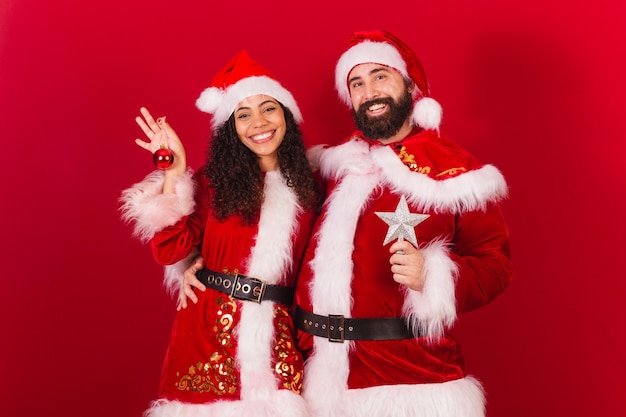 Pareja brasileña vestida para navidad santa claus momia claus sosteniendo decoración navideña estrella aprobada mujer negra y hombre caucásico