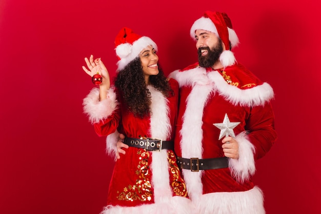 Pareja brasileña vestida para navidad santa claus momia claus sosteniendo decoración navideña estrella aprobada mujer negra y hombre caucásico