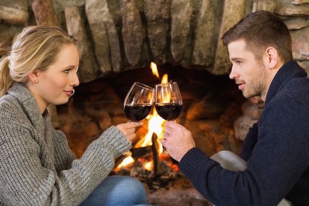 Pareja brindando copas delante de la chimenea encendida