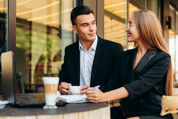 Pareja en la cafetería trabajando en la computadora portátil durante la cena y mirándose.- Imagen