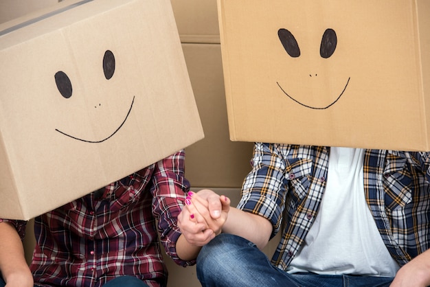 Pareja con cajas de cartón en la cabeza con cara sonriente.