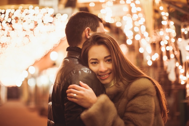 Pareja en la calle antes de Navidad. Telón de fondo de decoraciones de luces bokeh