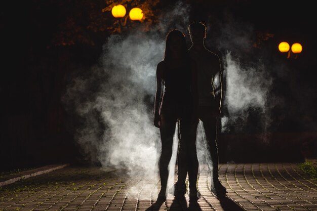 La pareja se para en el callejón oscuro sobre el fondo de humo. Noche