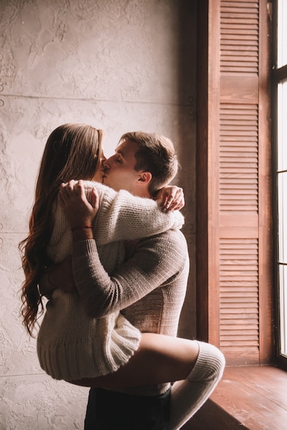 Pareja en la cama en el dormitorio. Interior oscuro Año Nuevo y Navidad. Abrazos y besos. Amor. Suéter blanco y medias altas. Encuentro romántico Una cita amantes.